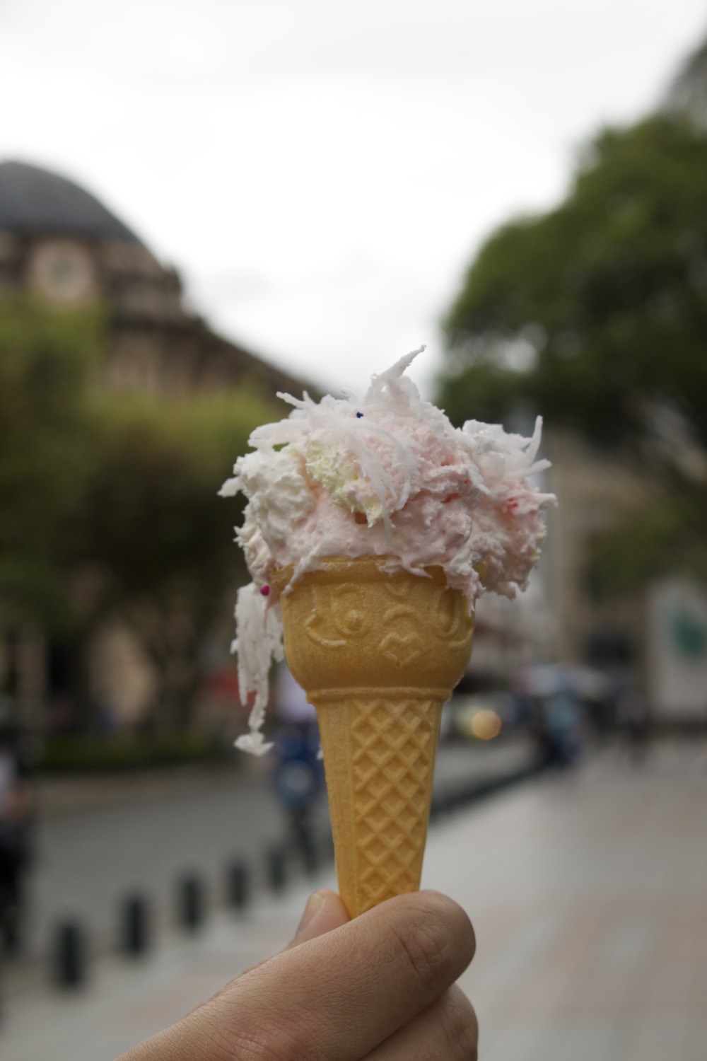 Mano sosteniendo un cono pequeño con espuma rosada y coco rallado