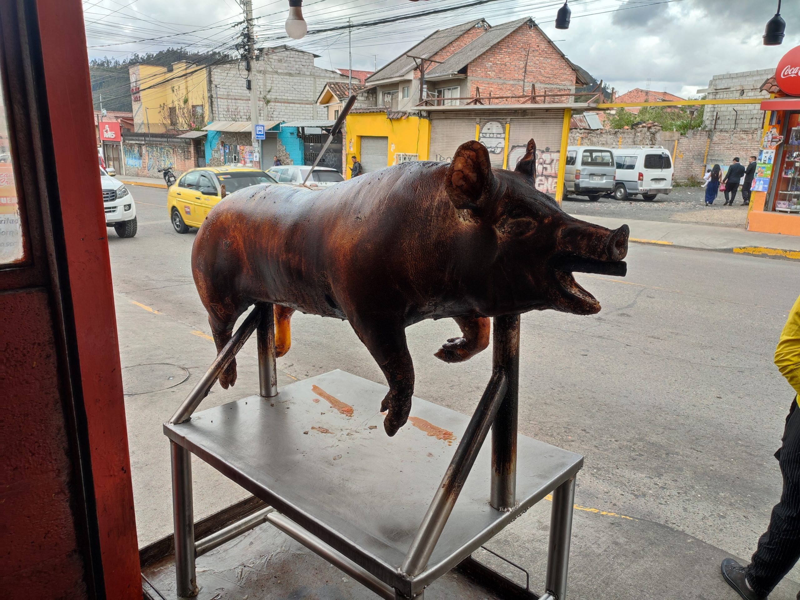Cerdo entero asado sobre un soporte metálico junto a una calle concurrida